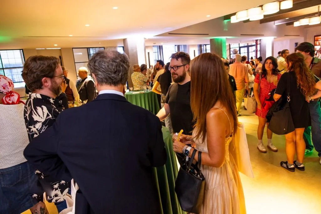 People socializing at a lively indoor event or party with a diverse crowd, standing around high tables, engaging in conversations.