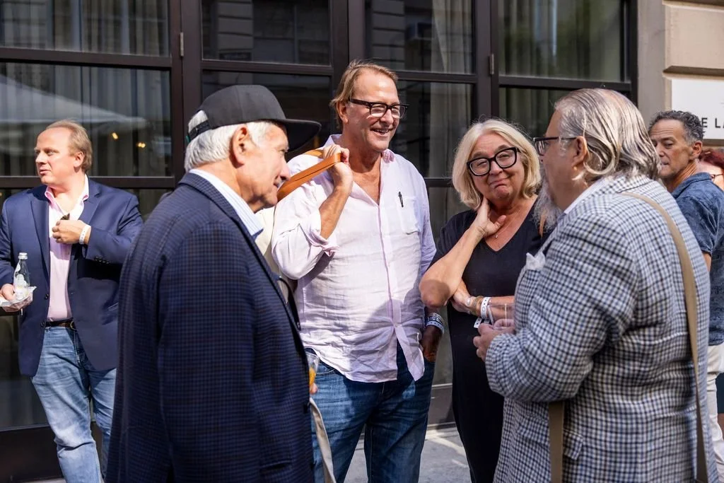 People having a conversation outdoors in front of a building, with some holding drinks.