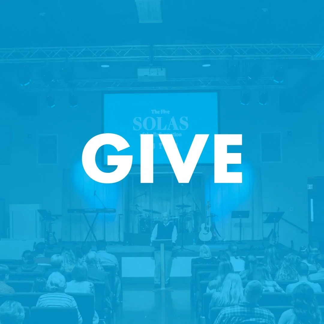 A speaker on stage in front of a seated audience, with a large screen behind him displaying 'The Five SOLAS'. The word 'GIVE' is overlaid in large white text.