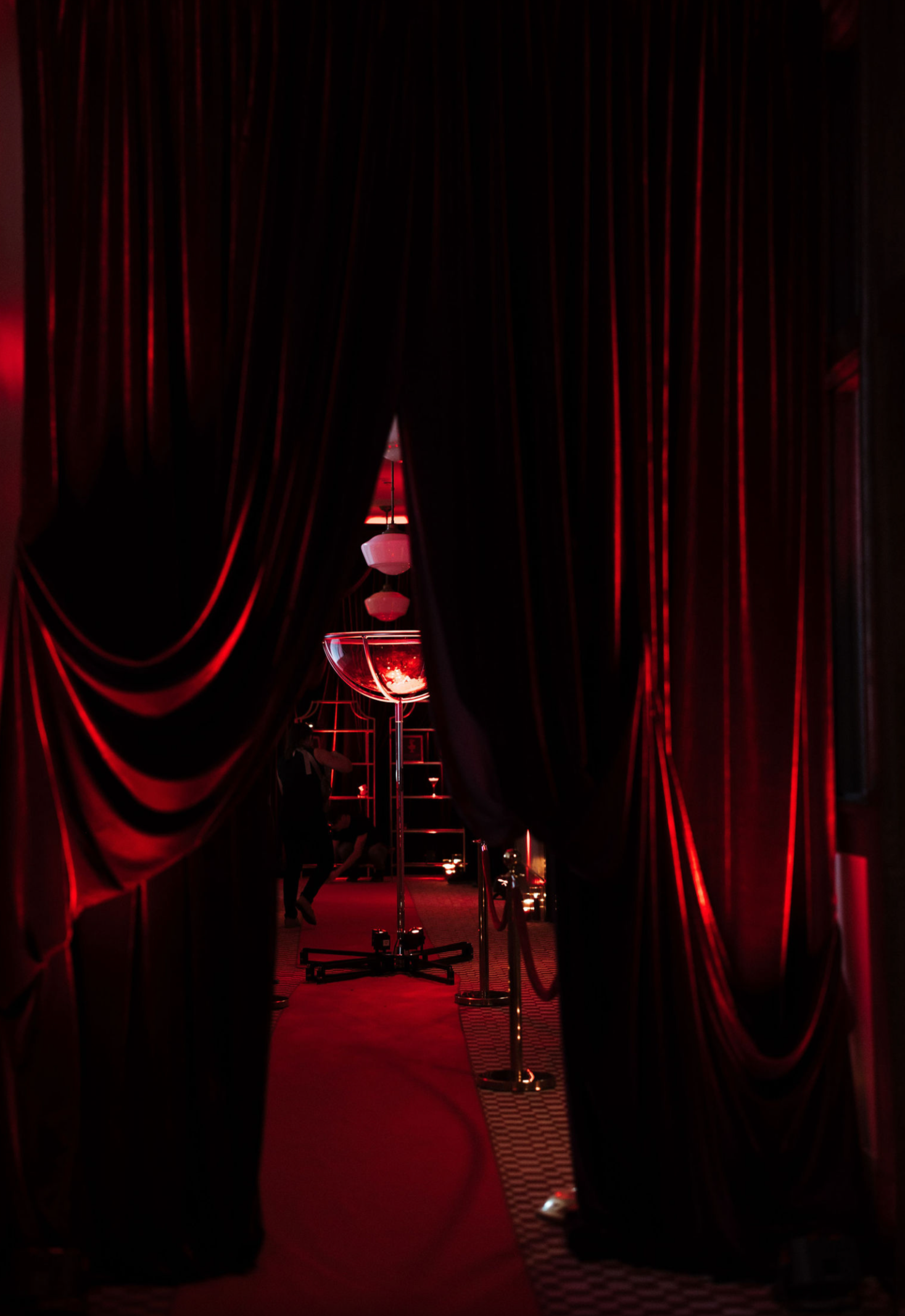 Red velvet curtains opening to a dimly lit venue with a large martini glass and hanging lamps, creating an elegant, upscale atmosphere.