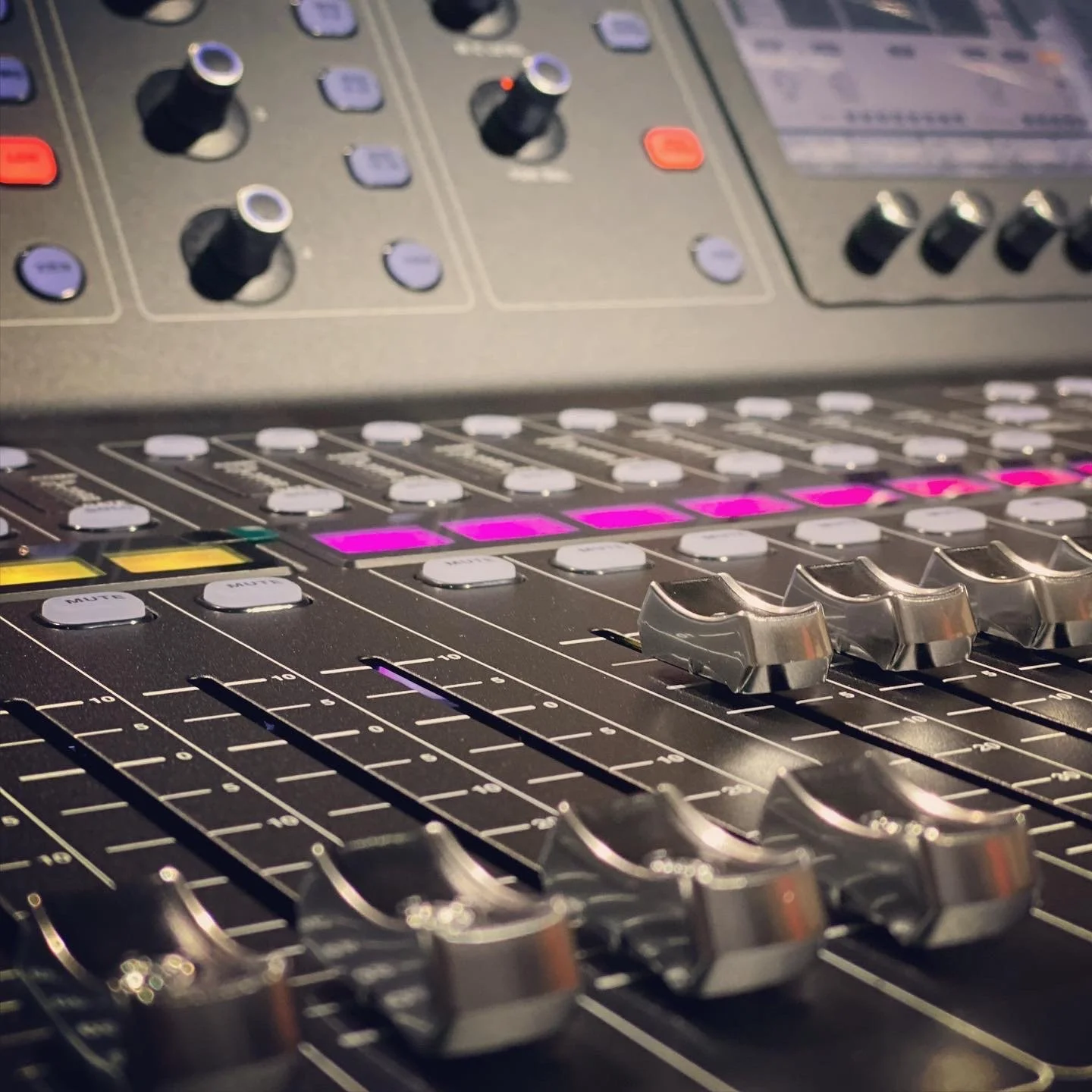 Close-up of a professional audio mixing console with multiple knobs, faders, and buttons in various colors.