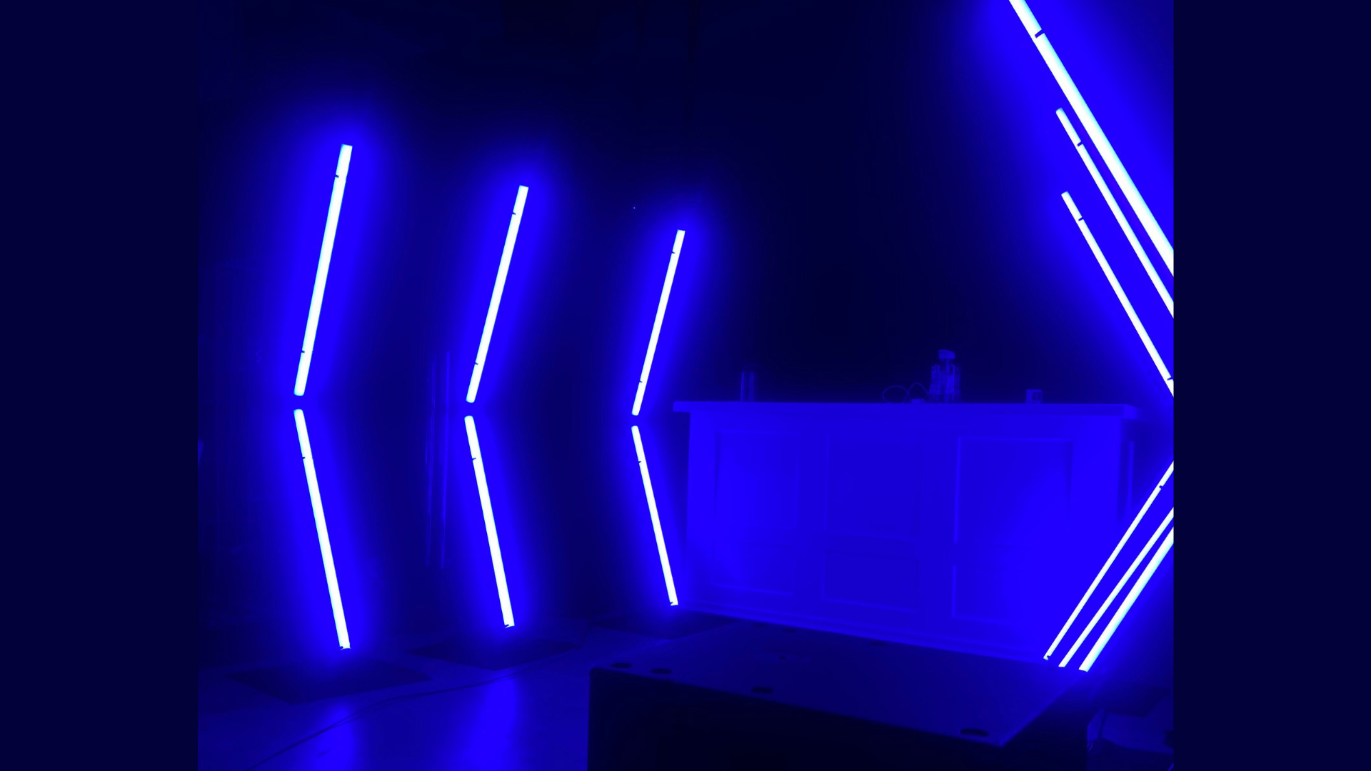 Room illuminated with blue neon LED lights arranged in angled strips on the walls, with a counter or bar area on the right side.