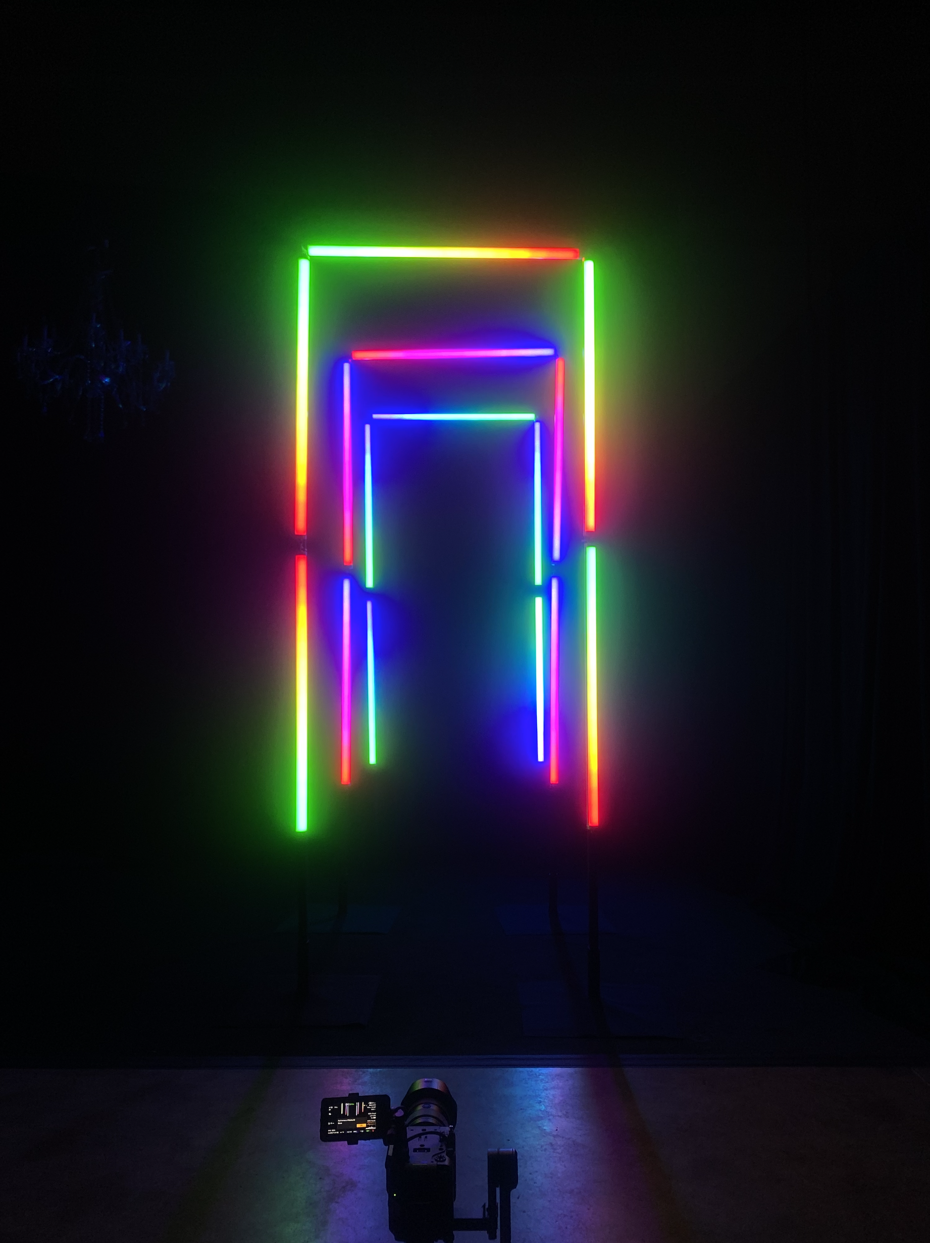 Colorful neon light installation with concentric rectangular frames in rainbow colors against a dark background.