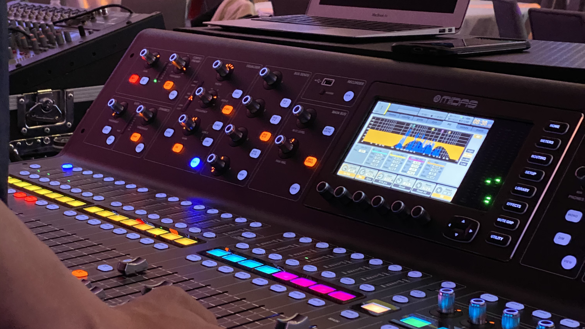 A digital music mixing console with illuminated buttons, knobs, and a touchscreen display showing a colorful sound waveform.