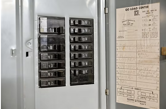Electrical breaker box with switches and a load center sheet with handwritten notes attached to the inside of the electrical panel door.