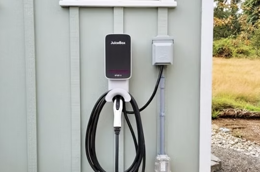 Electric vehicle charging station mounted on a light green exterior wall outside, with a charging cable and connector hanging from it.