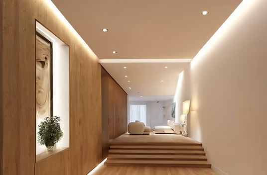 Modern hotel room with a bed on a raised platform and steps leading up to it, decorated with minimalistic furniture and artwork. Soft lighting illuminates the room.