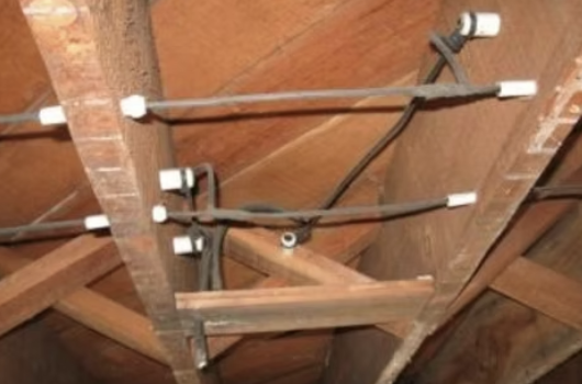 Electrical wiring and conduit pipes installed in an attic ceiling space.