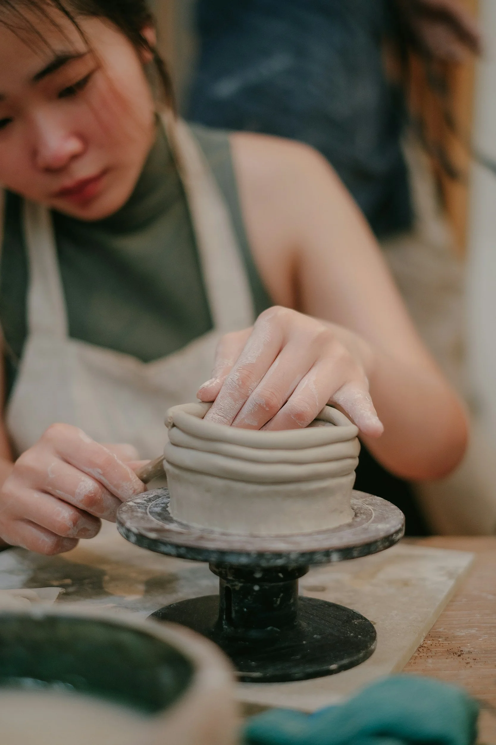 A person shaping clay on a pottery wheel, with hands covered in clay and focusing on molding the pottery.
