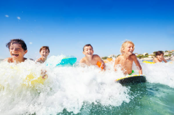 Group of children surfing and playing in the ocean with smiles on their faces.