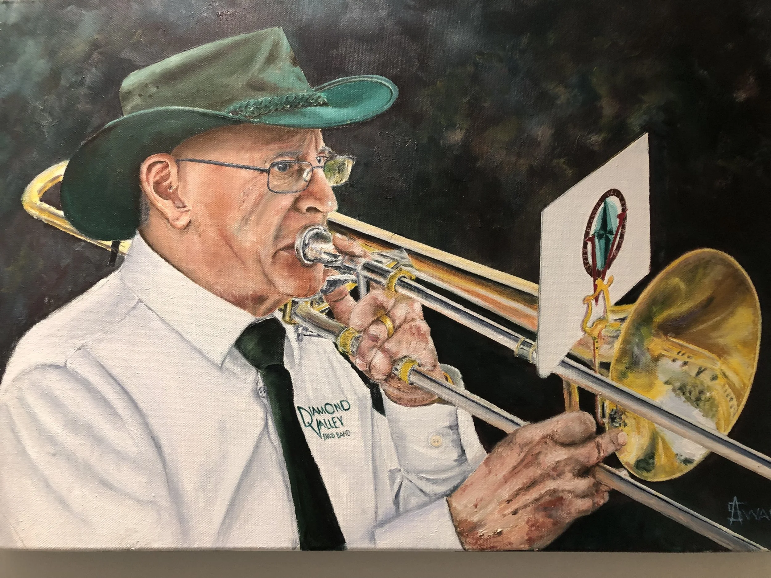 Painting of a man wearing glasses and a green hat, playing a trombone. He is dressed in a white shirt with a name tag that reads 'Diamond Valley Brass Band' and is playing the trombone in front of a music stand with the logo of the band.