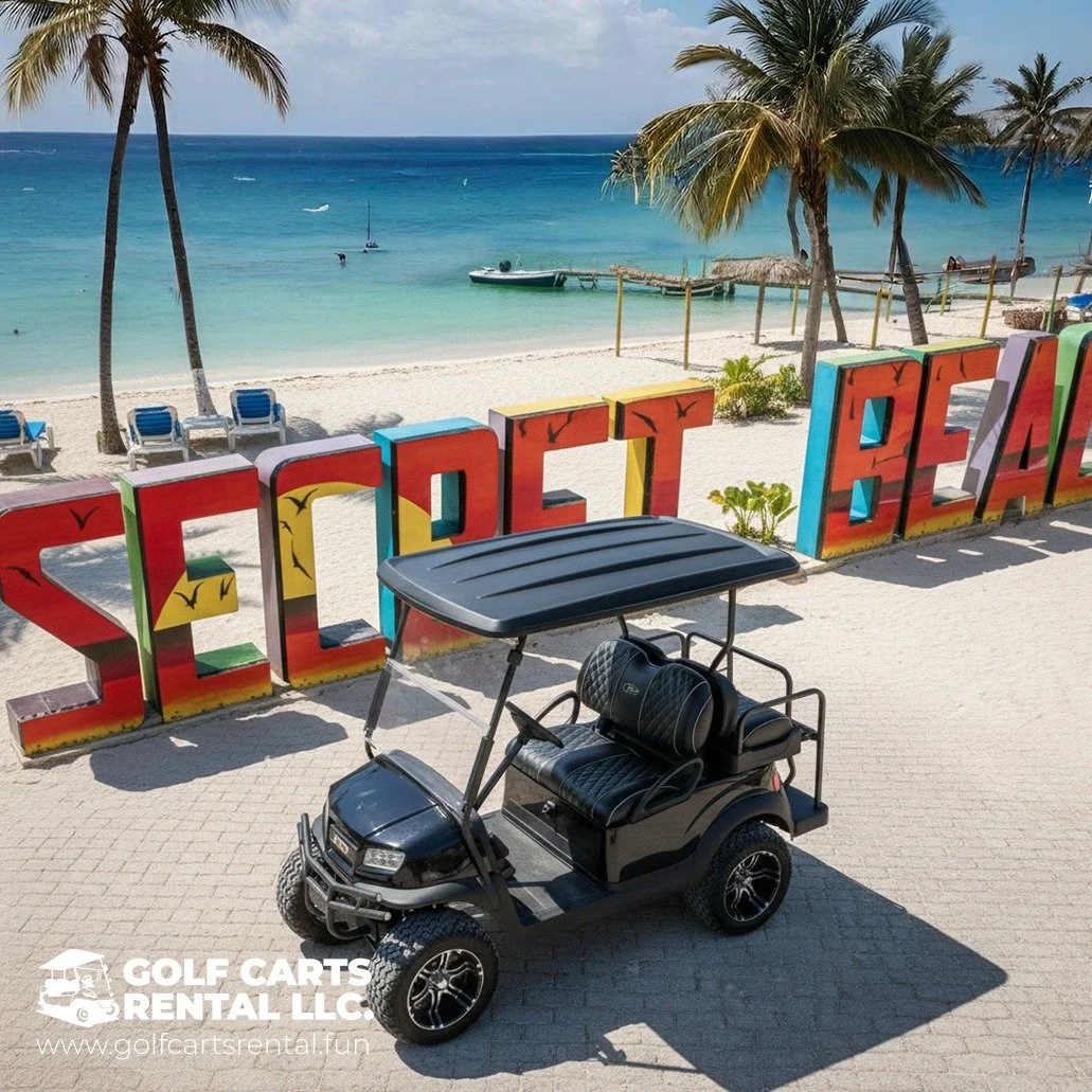 Colorful 'SOLUTION BEACH' sign on white sandy beach with palm trees, boats, and turquoise ocean in the background, with a black golf cart in the foreground.