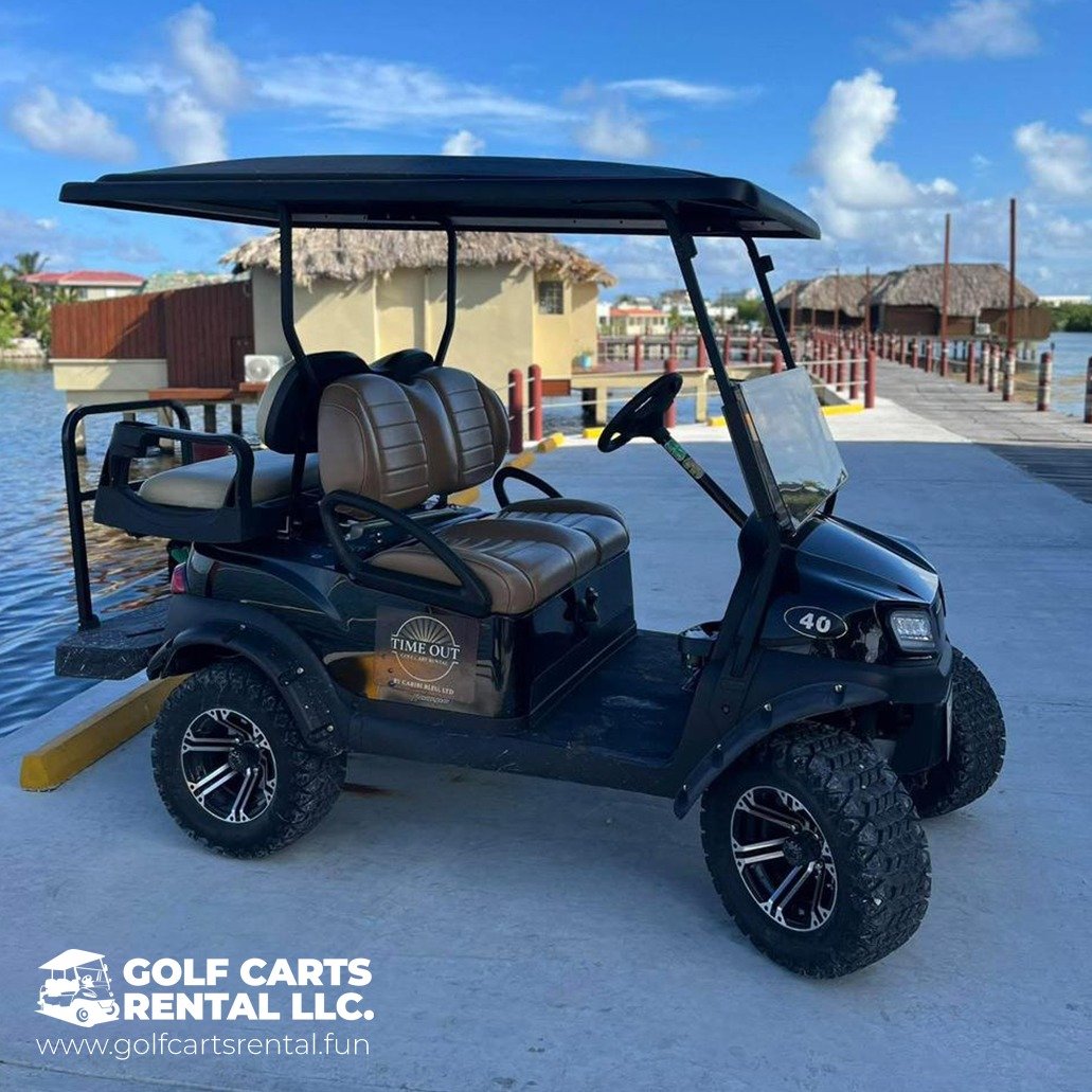 A black golf cart with a roof and brown leather seats parked on a concrete pier near water, with overwater bungalows and a bright blue sky in the background.