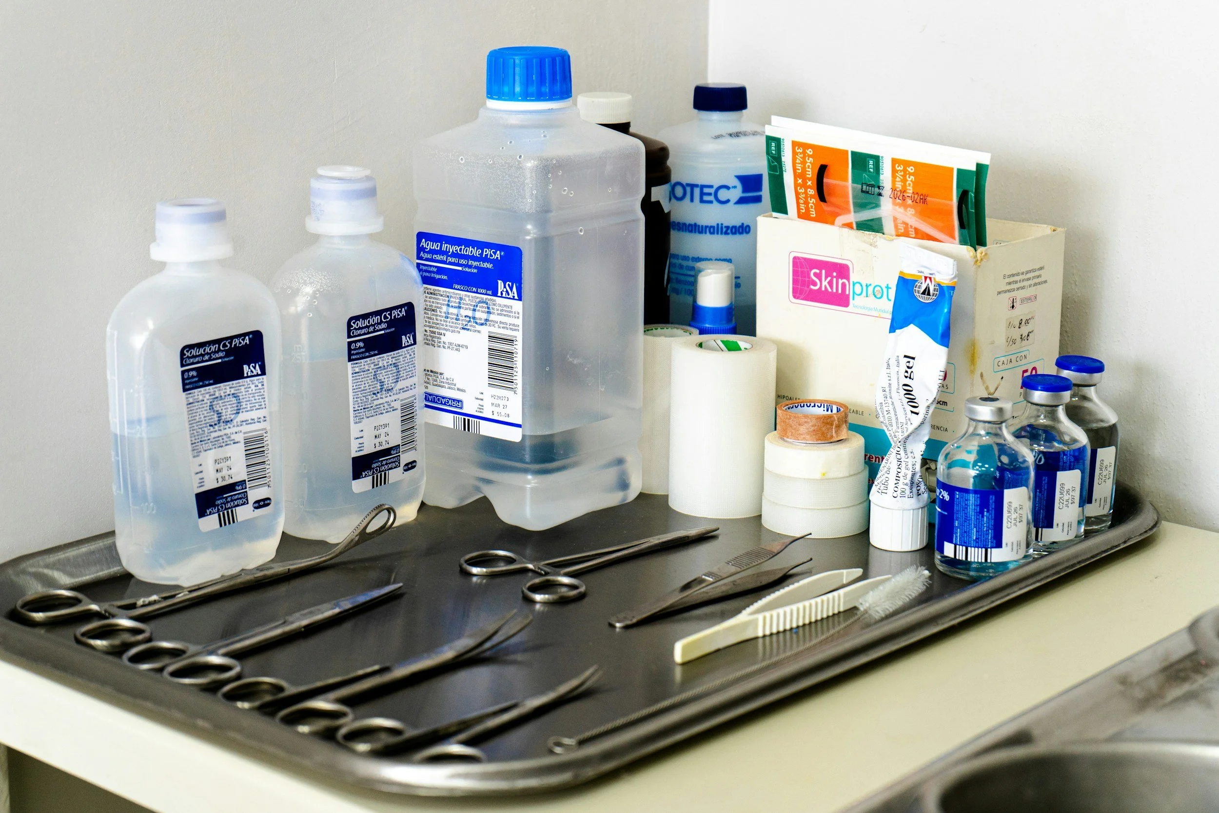 Medical instruments, bottles of antiseptic solution, bandages, and medical supplies on a tray in a clinical setting.