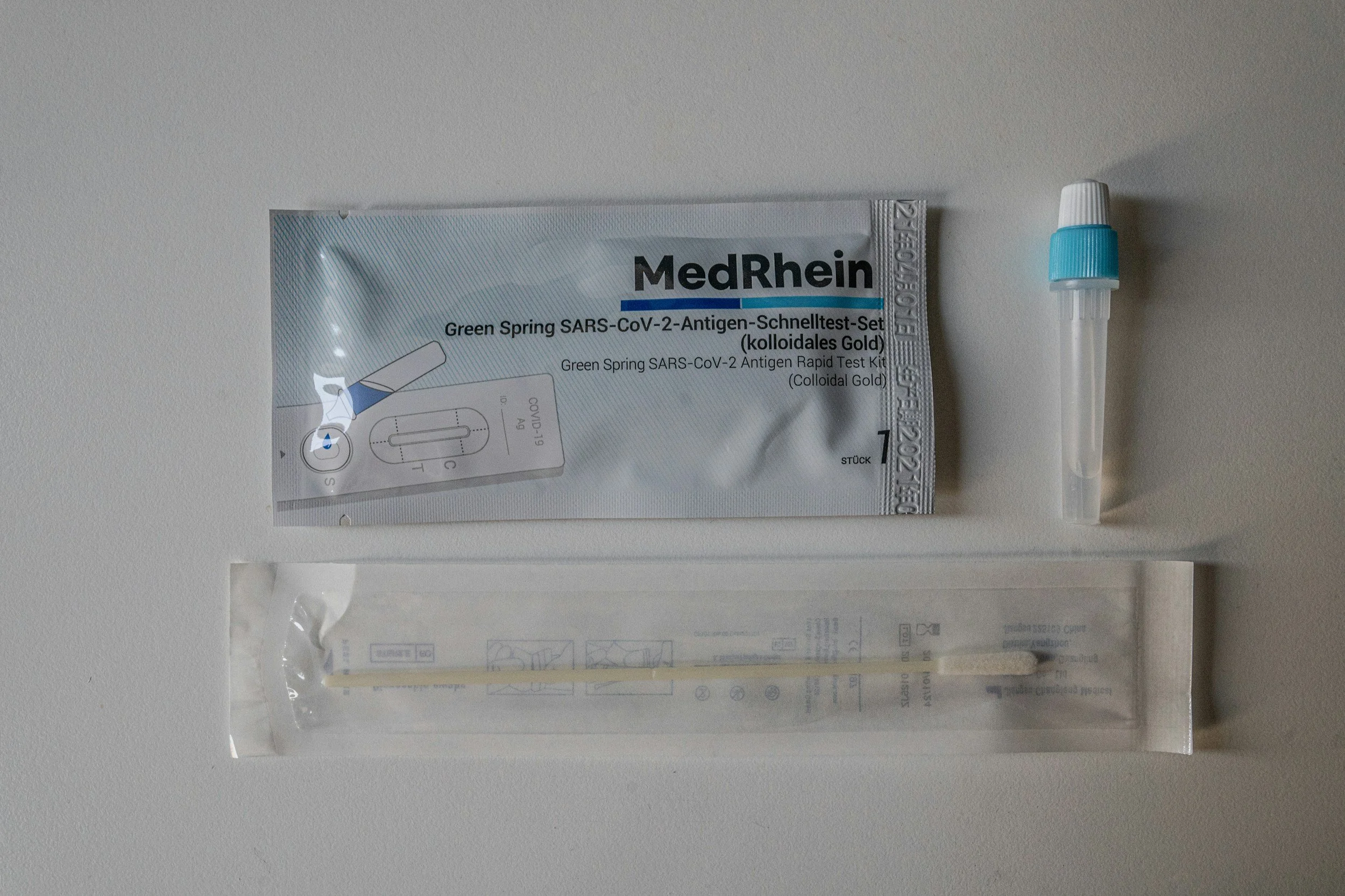 Medical testing kit package, a swab in a sealed plastic wrapper, and a small dropper container on a white surface.