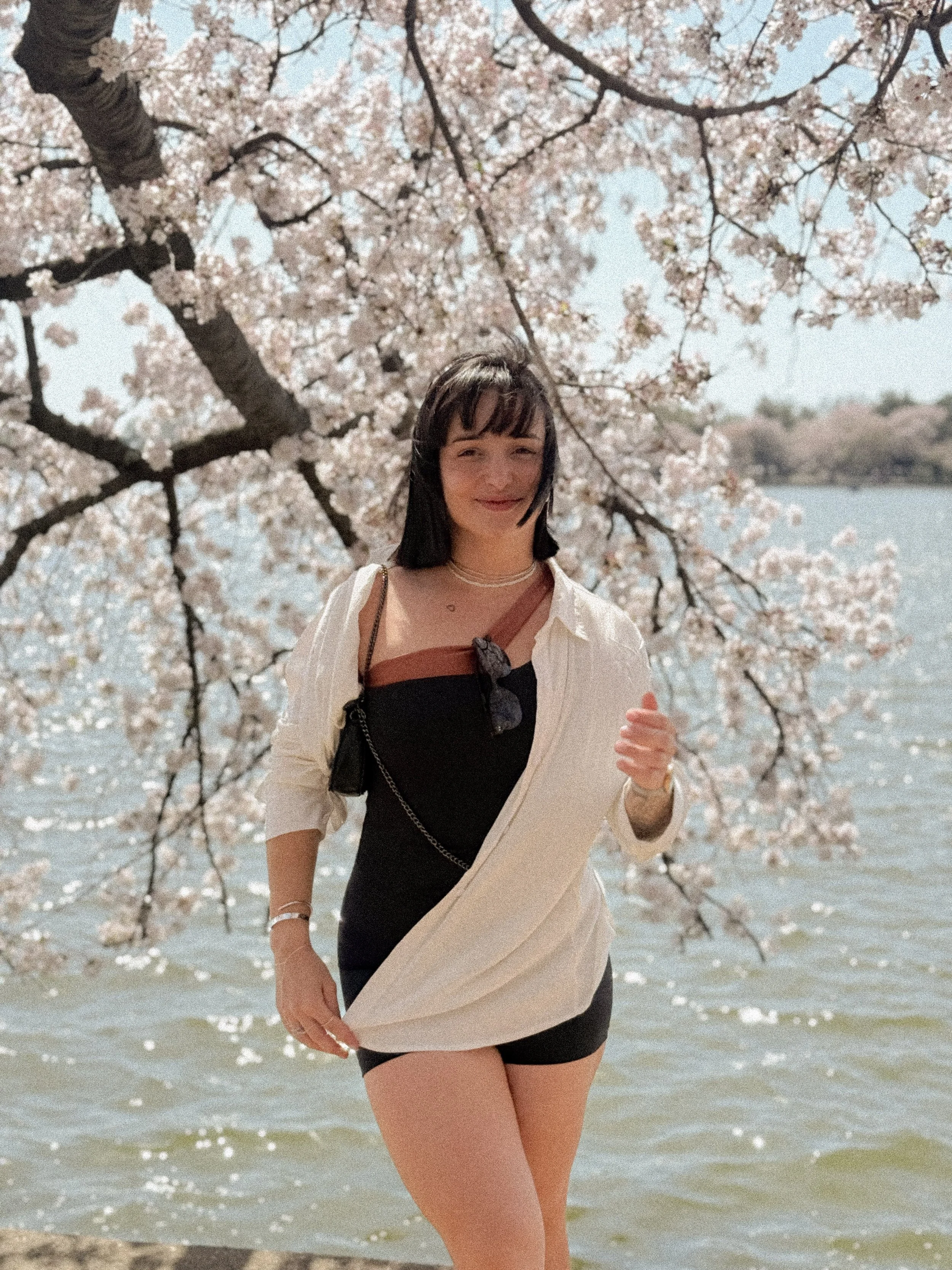Larissa Mara Vale sorrindo ao lado de uma cerejeira em flor próximo a um lago - Conteúdo sobre presença e apreciação estética.