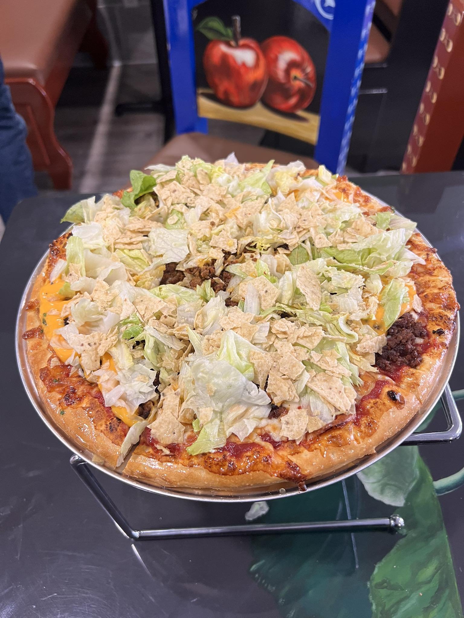 Large taco pizza topped with shredded lettuce, cheese, ground beef, and crushed tortilla chips, served on a metal tray.