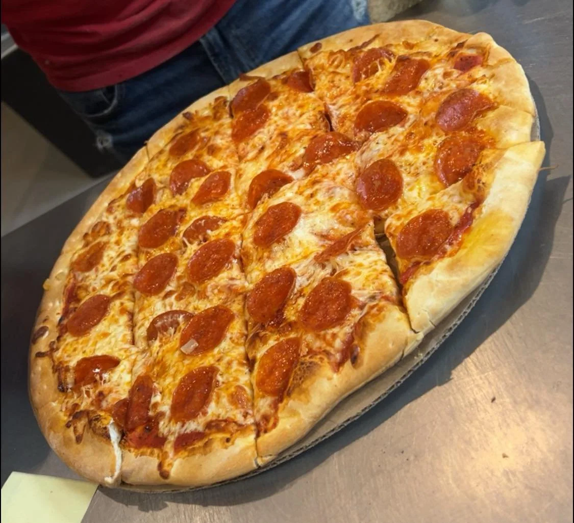 Large pepperoni pizza on a black tray with a golden crust, melted cheese, and slices of pepperoni.