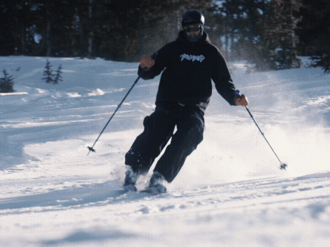 Person skiing down a snowy slope in a winter landscape with trees in the background.