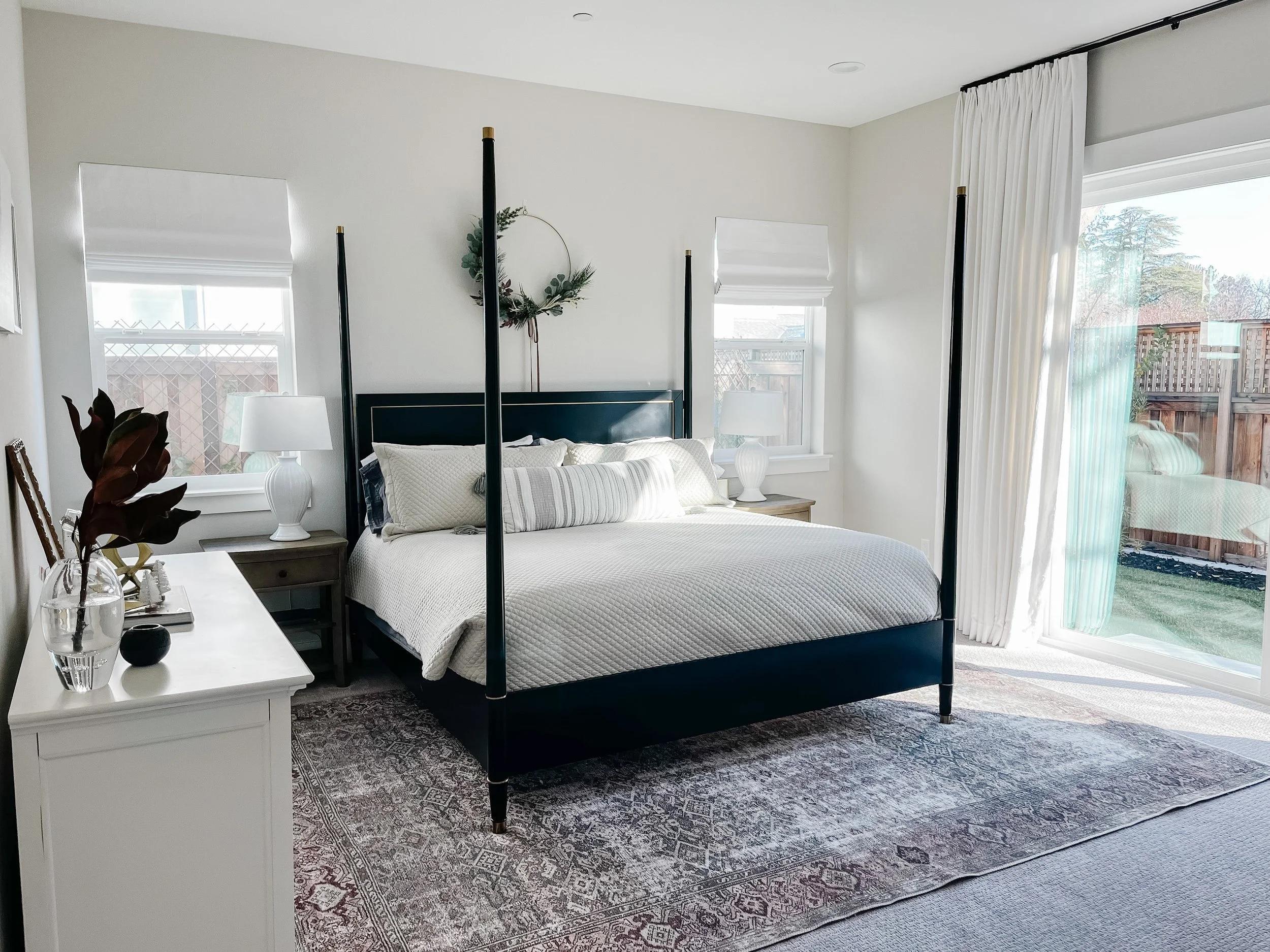 White calm primary bedroom with French-inspired black four-poster bed with brass accents and vintage rug--Casa Limones interior design