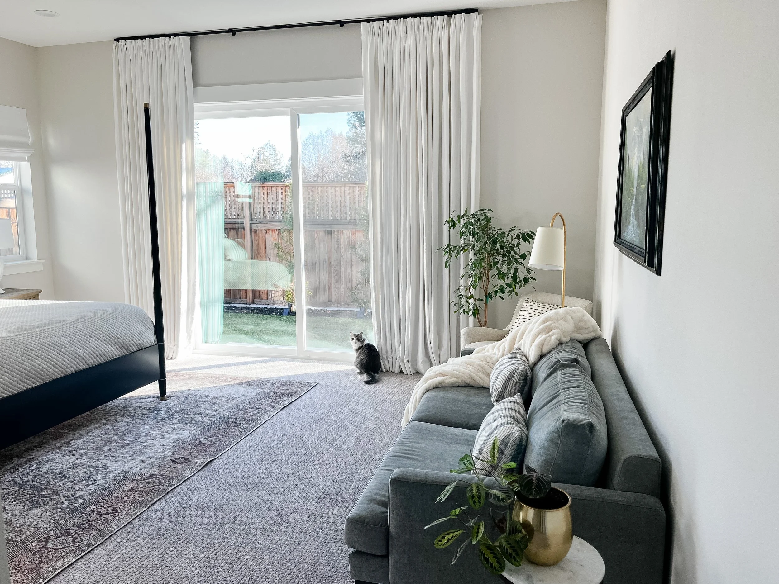 White calm primary bedroom with French-inspired black four-poster bed with brass accents, vintage rug, and grey sofa--Casa Limones interior design
