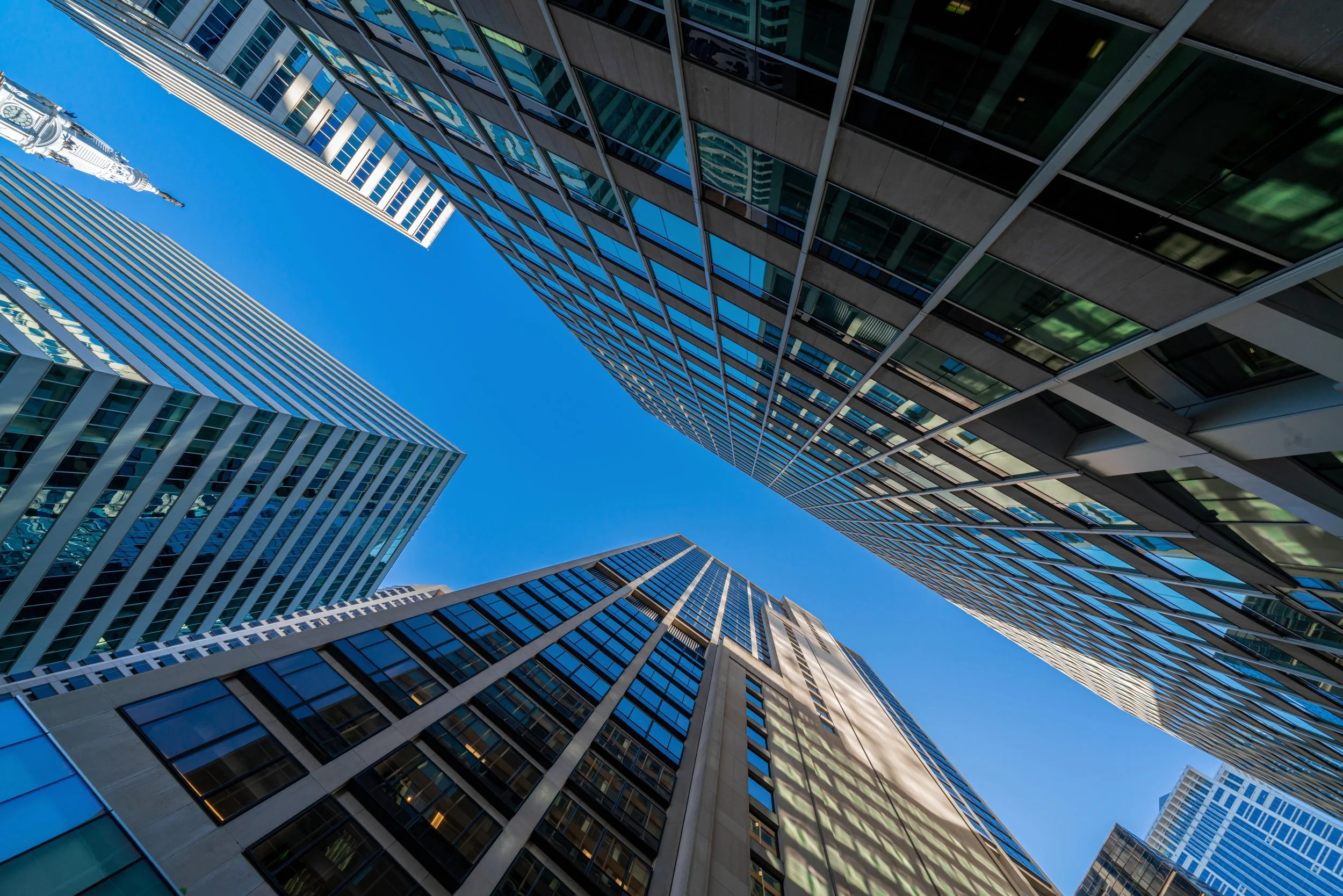 View looking up at tall skyscrapers with glass exteriors reflecting the blue sky in a cityscape.