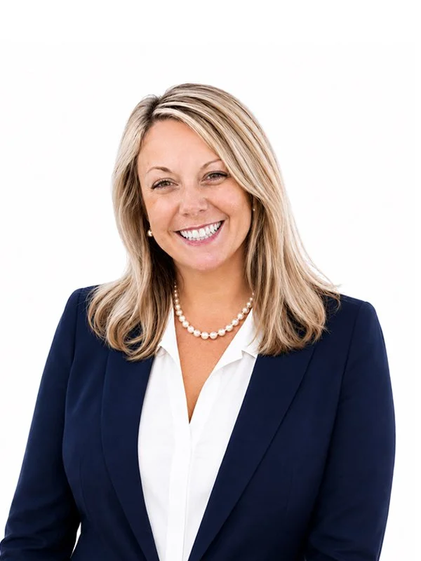 A smiling woman with blonde hair, wearing a navy blazer, white blouse, and a pearl necklace, against a plain white background.