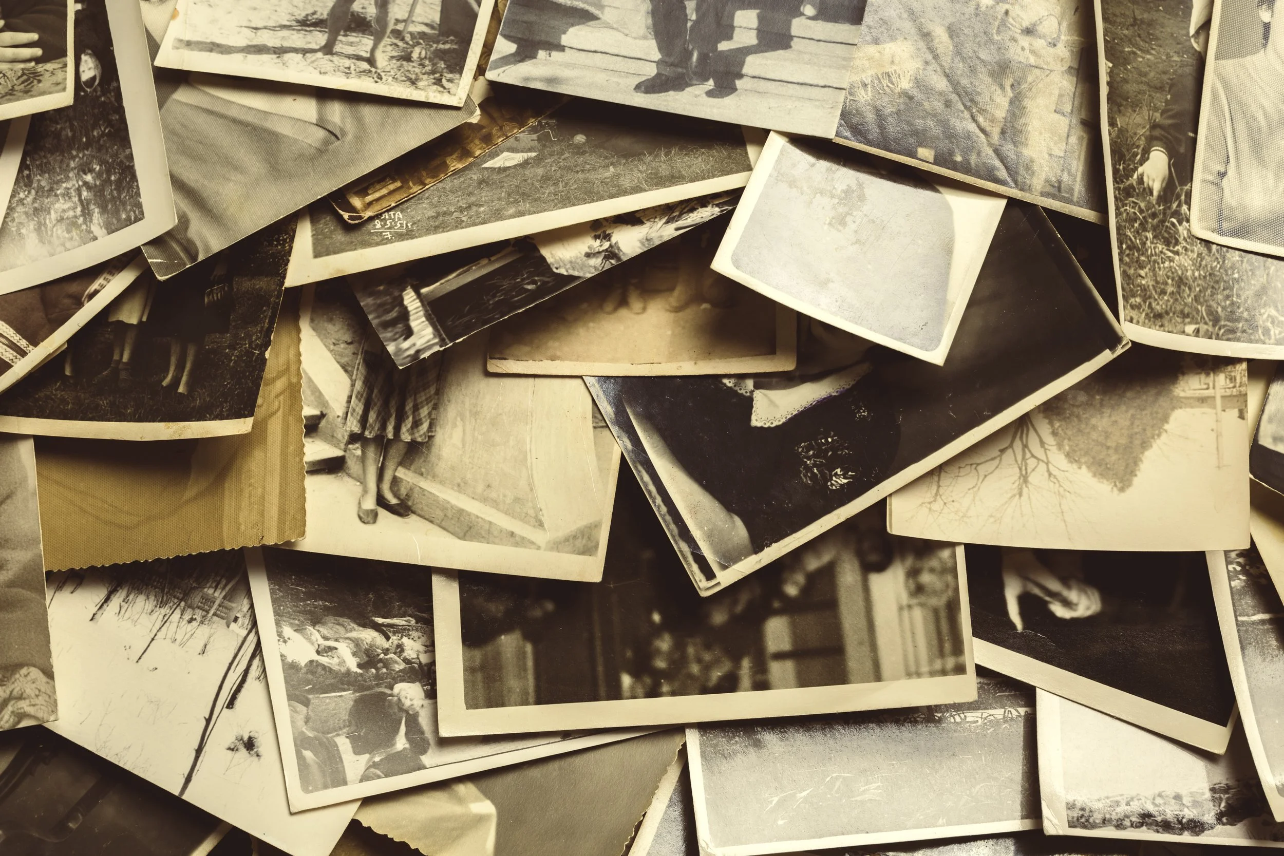 A pile of black and white photographs showing various scenes, including people, landscapes, and close-up details.
