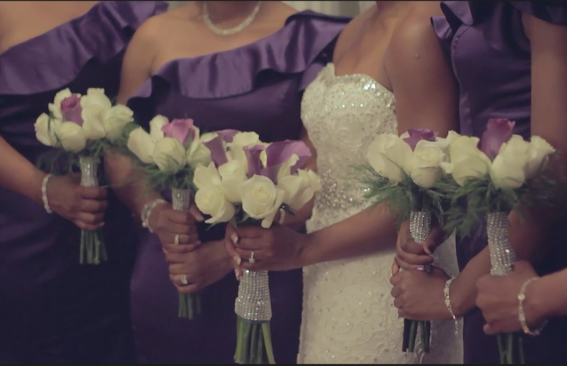Close-up of women holding bouquets of white and purple flowers during a wedding ceremony.