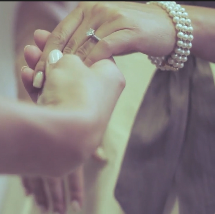 Close-up of two hands holding each other, one wearing a pearl bracelet and a ring, suggesting a bonding or ceremonial moment.