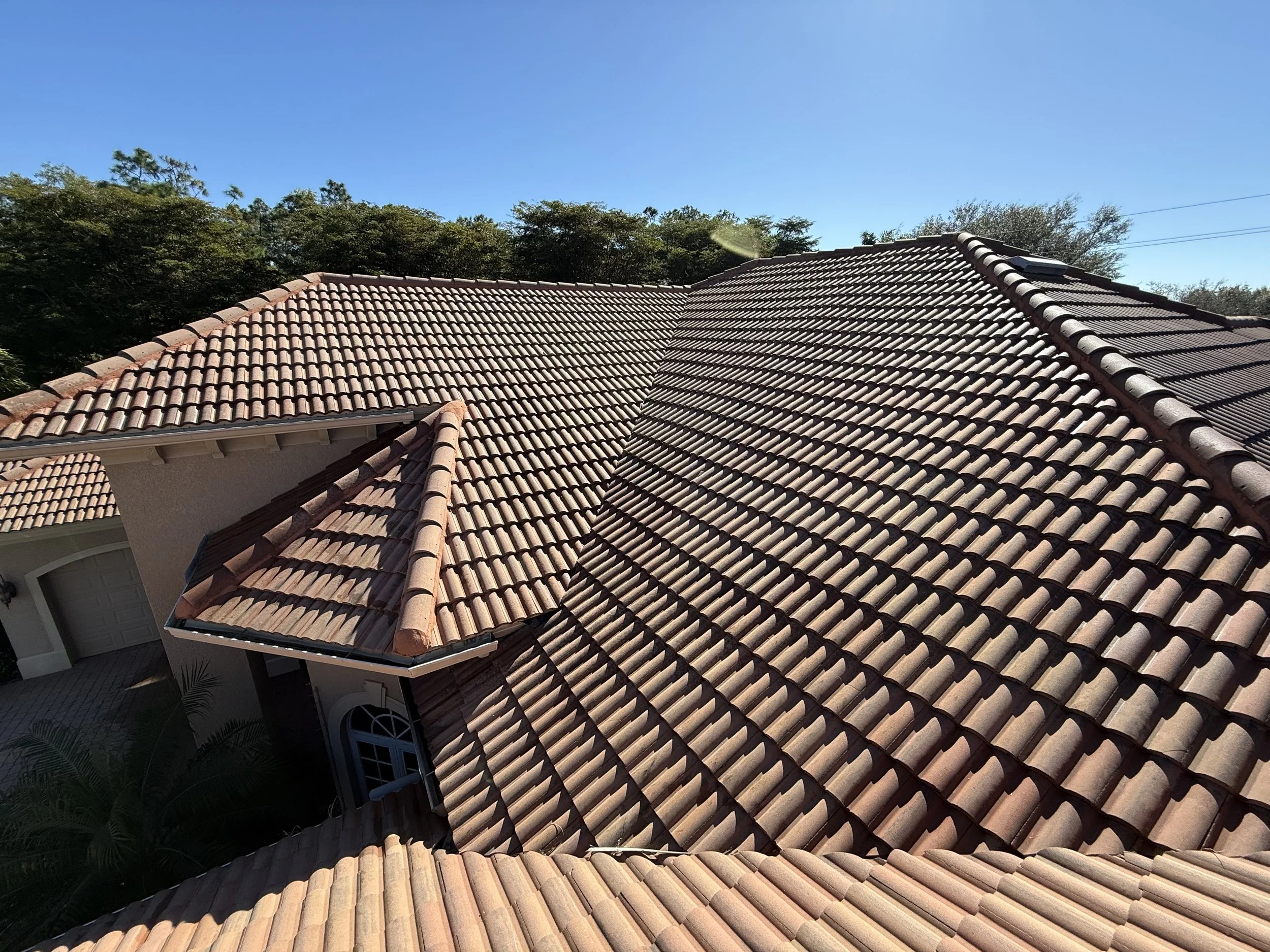 View of a house roof with red clay tiles and a small dormer window, under a clear blue sky.