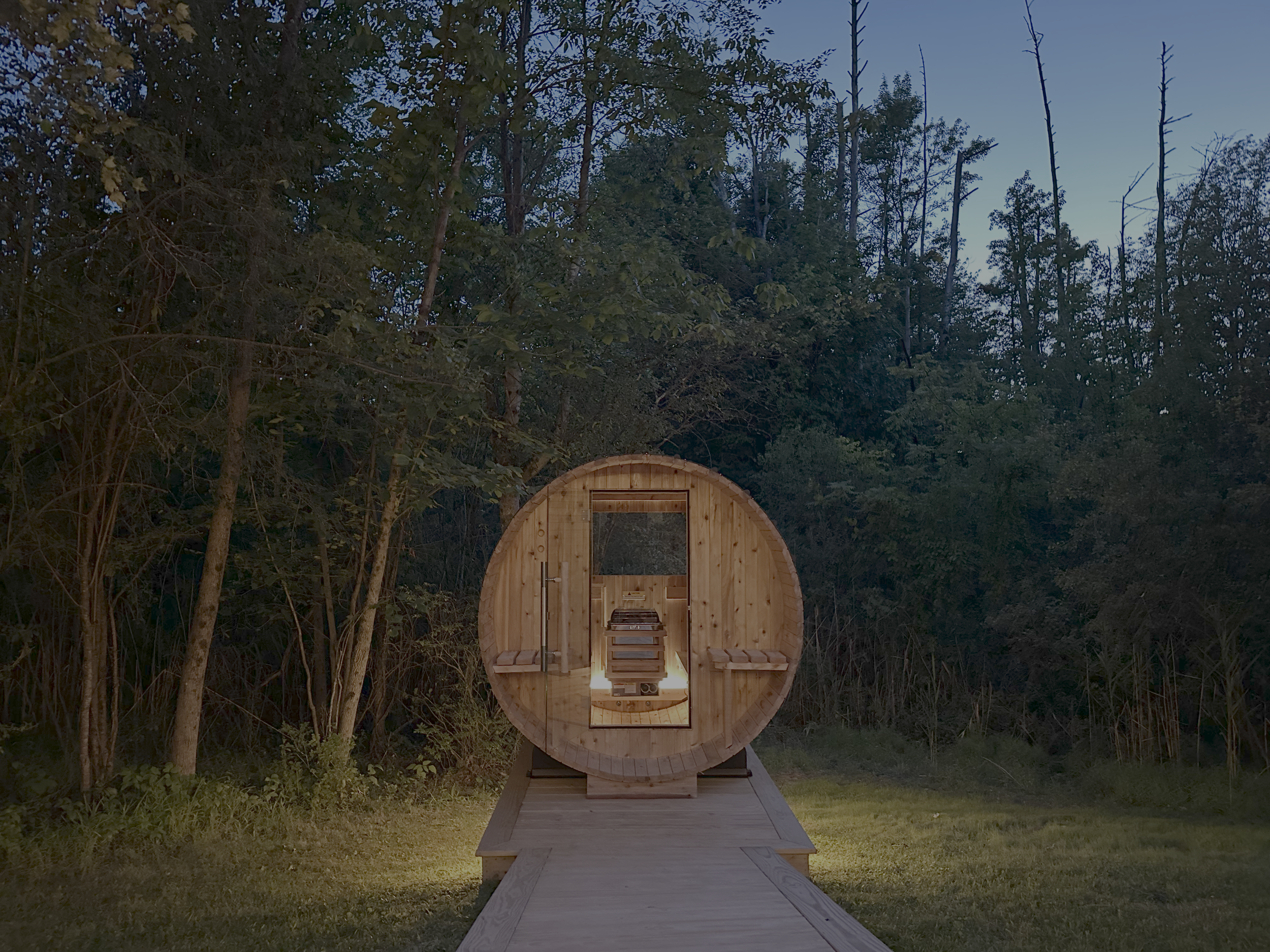 A wooden barrel-shaped sauna with an open door, situated outdoors on a wooden platform amidst trees at dusk.