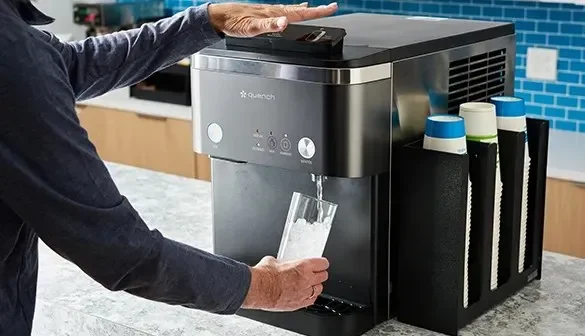 A person filling a glass with ice from a countertop ice machine.