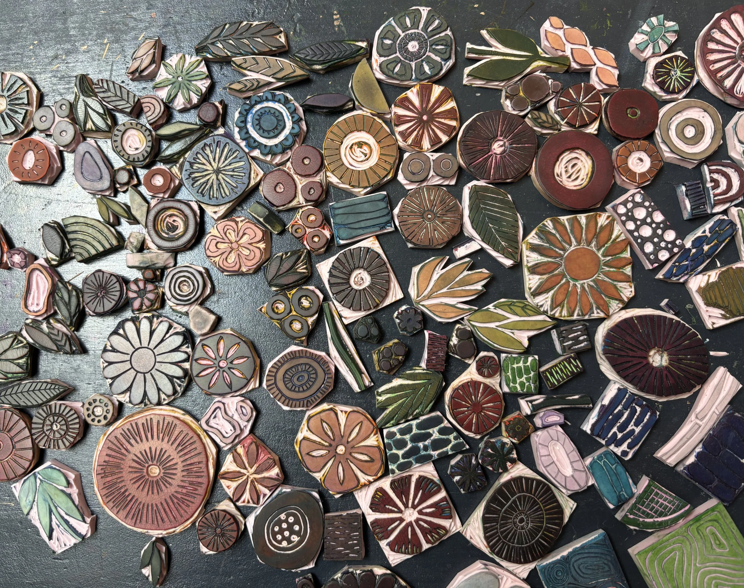 Colorful hand-carved stamps with various geometric and floral designs scattered on a dark surface.