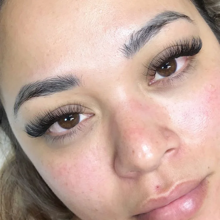 Close-up of a woman's face showing her makeup with natural eyebrows, long eyelashes, and lightly blushed cheeks.