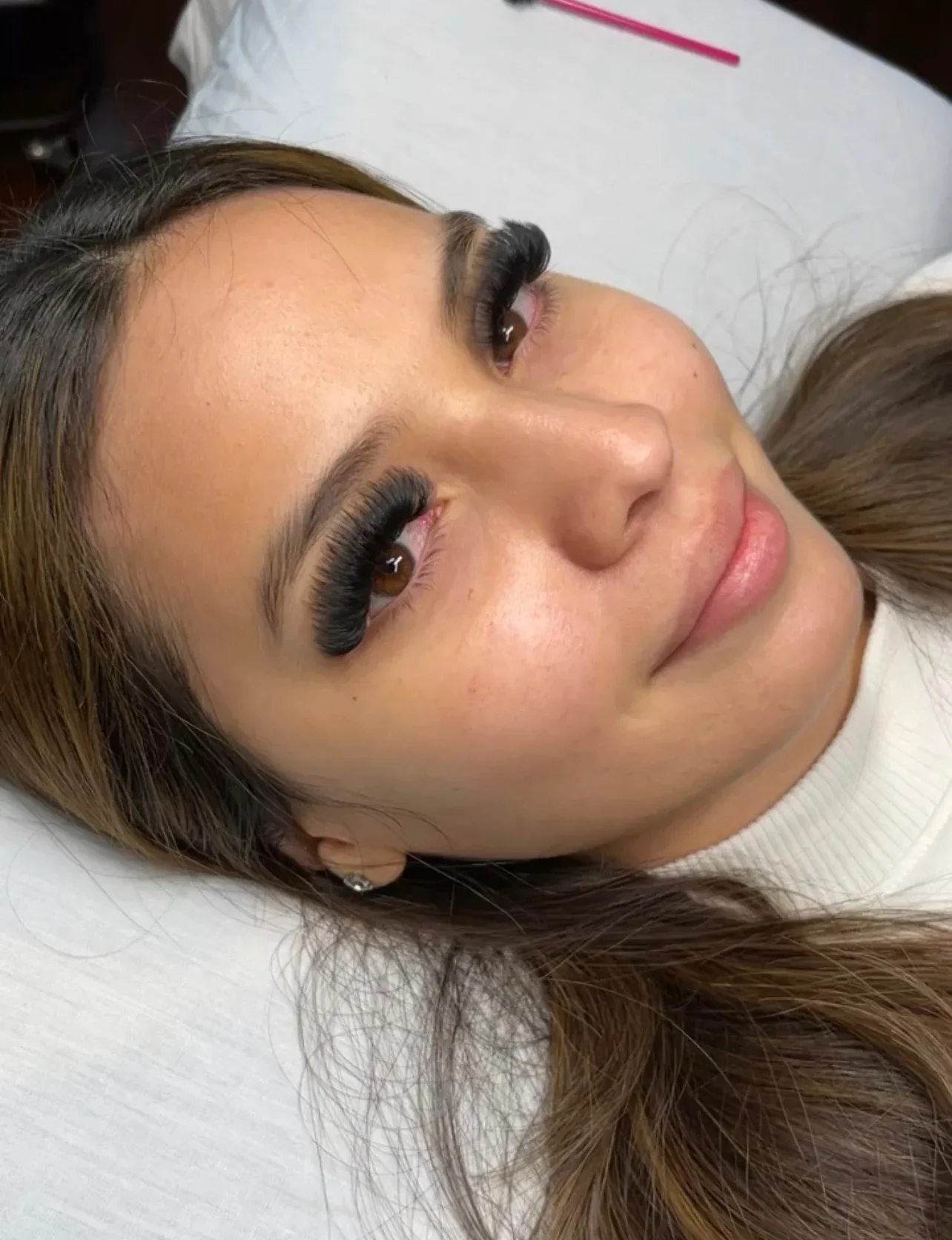 Close-up of a woman lying down, with long, wavy hair and eyelash extensions.