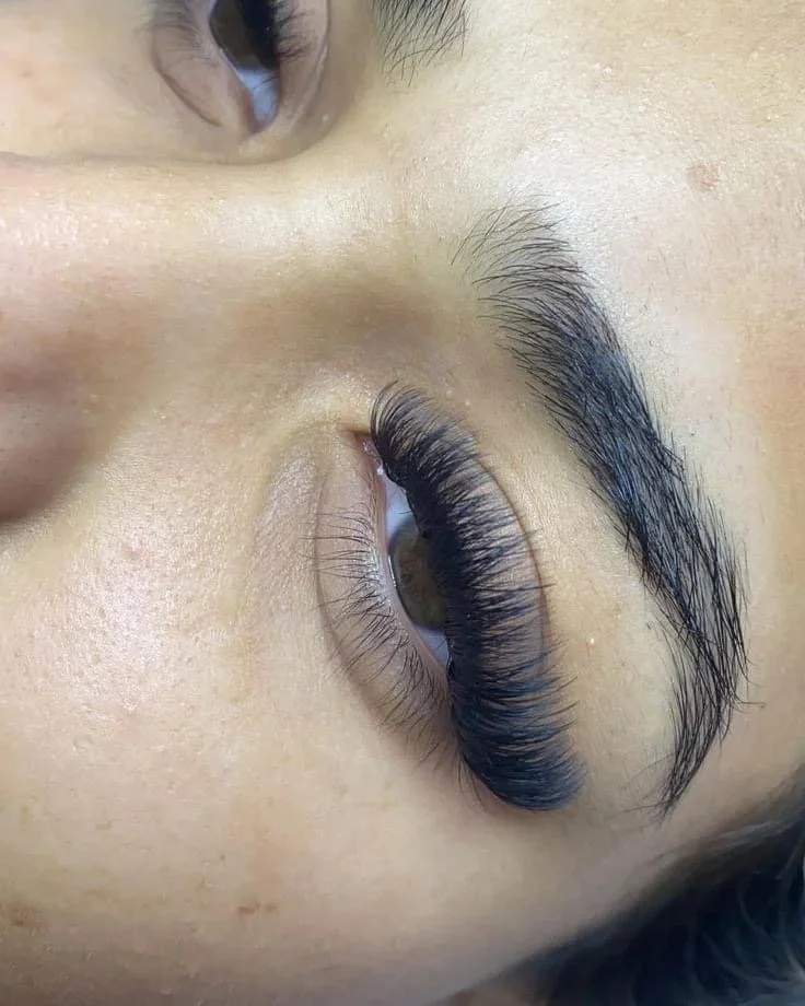 Close-up of a person's closed eye with long, thick, curled eyelashes and well-groomed eyebrows.