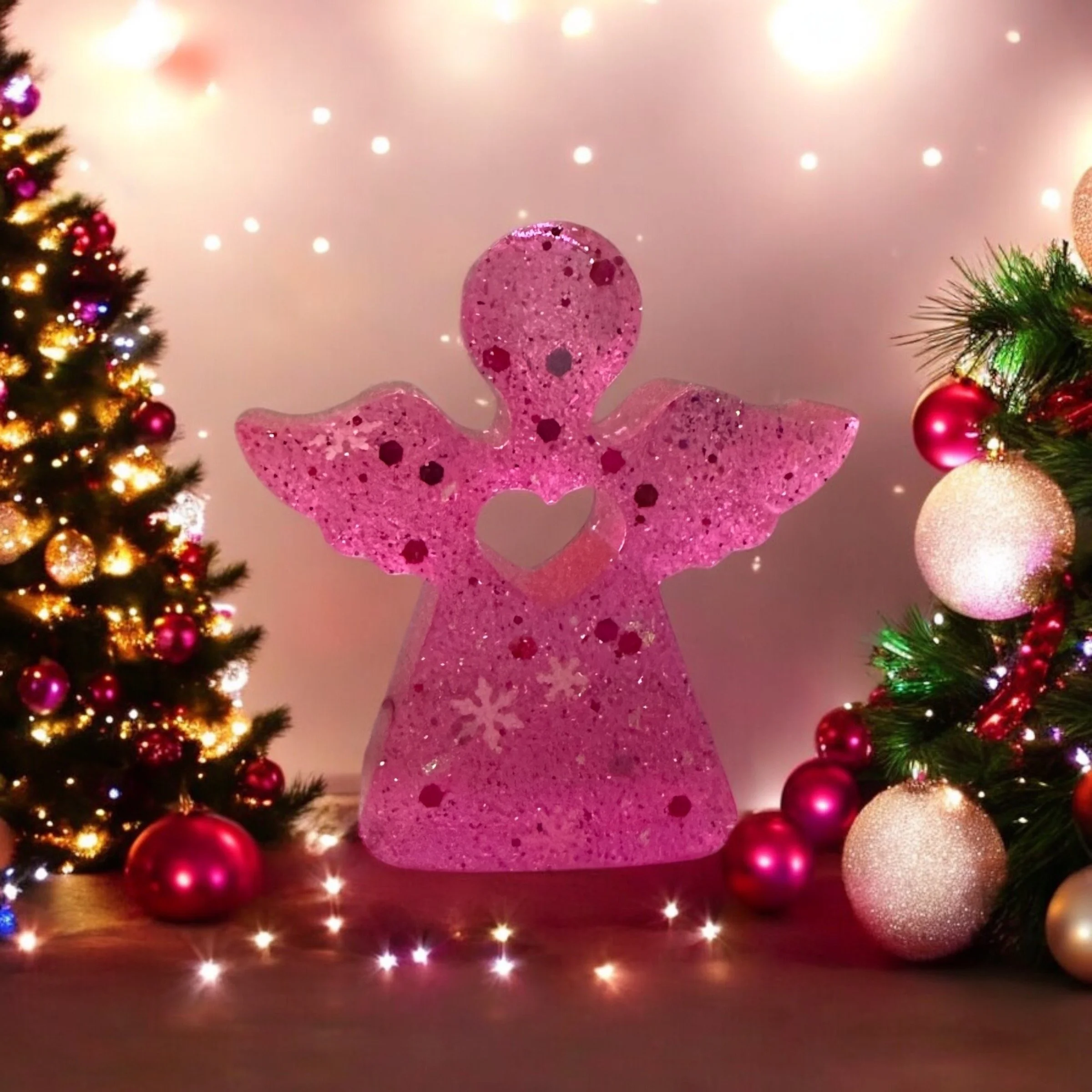 A pink angel Christmas decoration with a heart cutout in the center, surrounded by decorated Christmas trees with lights and ornaments.