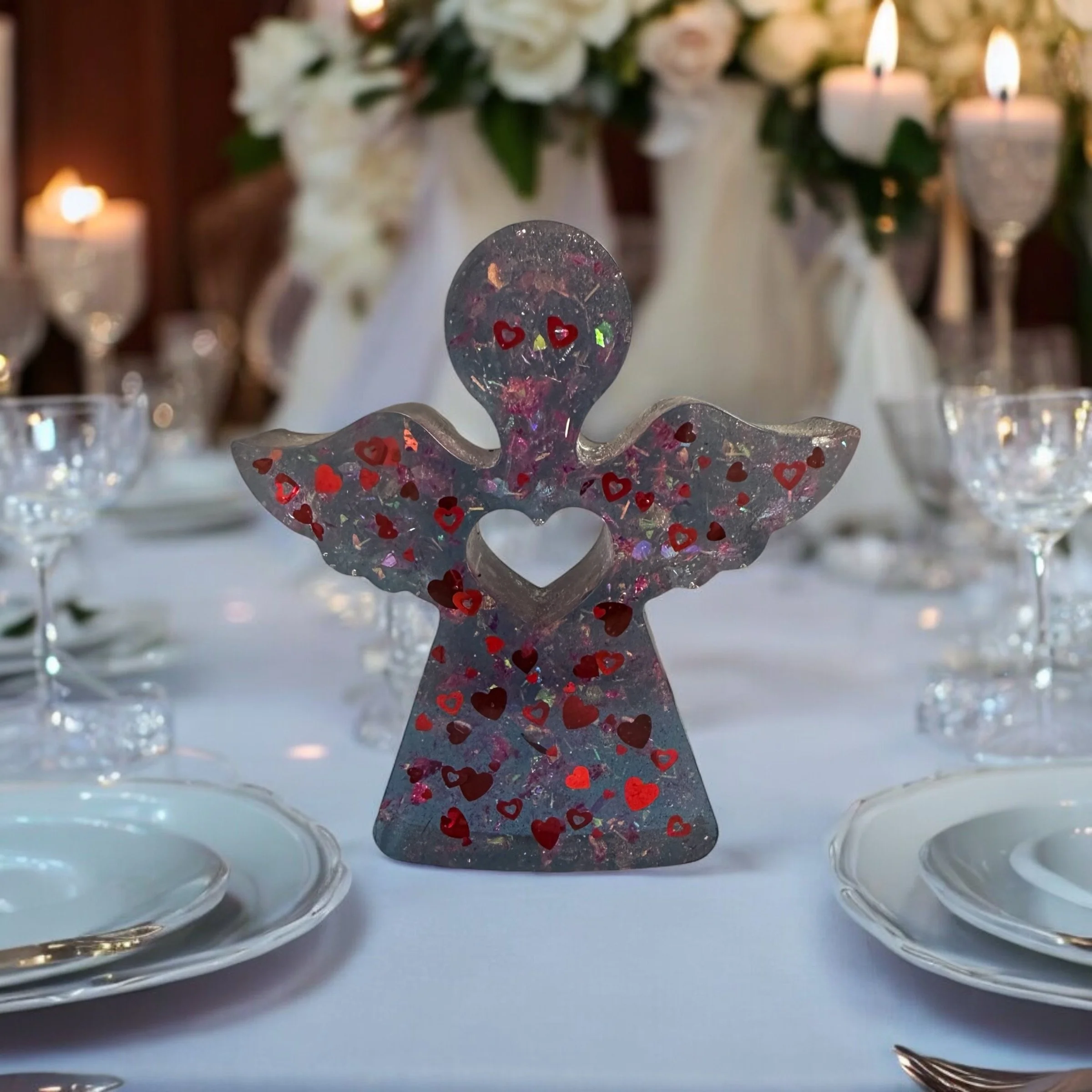 Decorative angel centerpiece with hearts on a dining table, surrounded by glassware and plates, with floral arrangements and candles in the background.