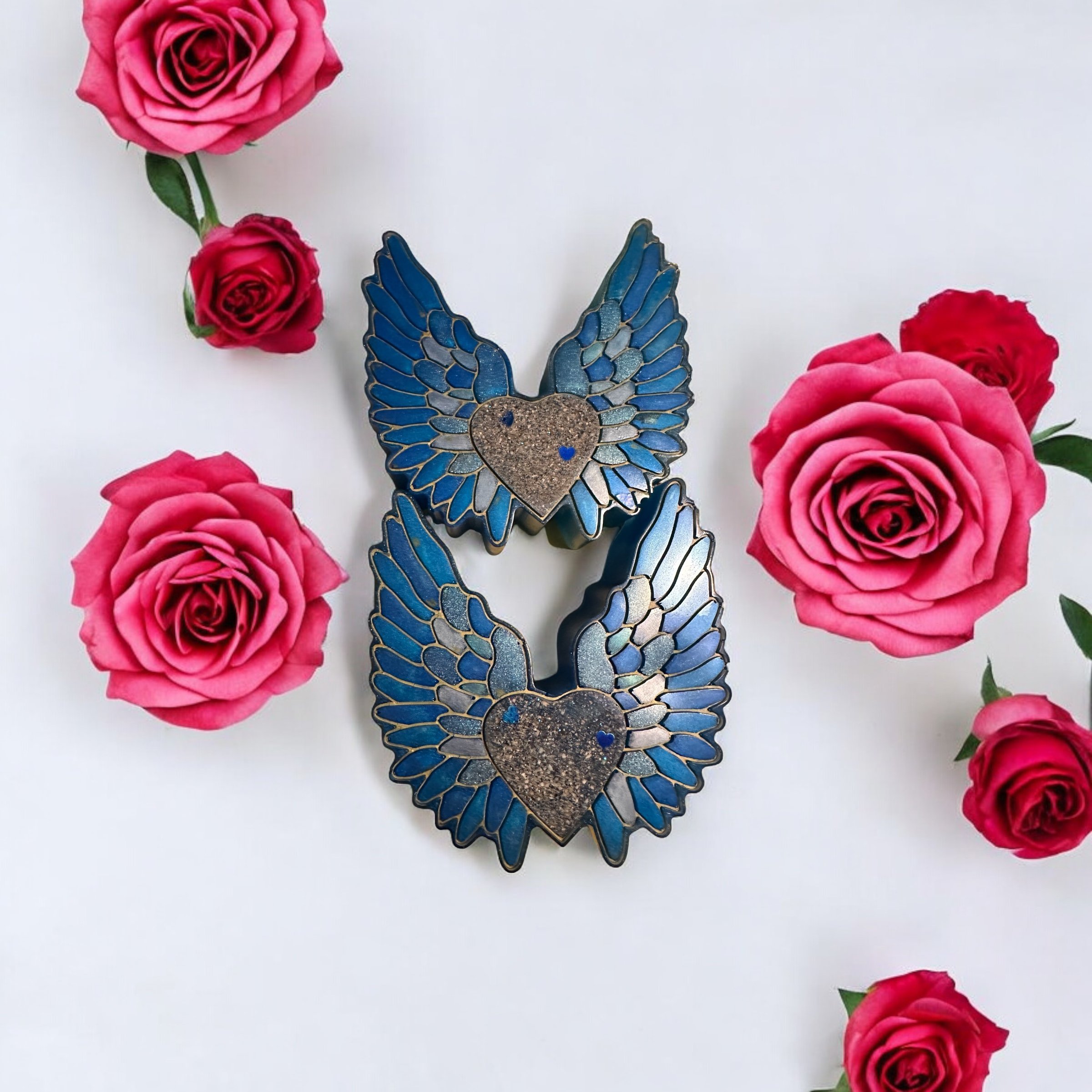 Two blue butterfly-shaped candles with glittering gold hearts on top, surrounded by pink roses on a white background.