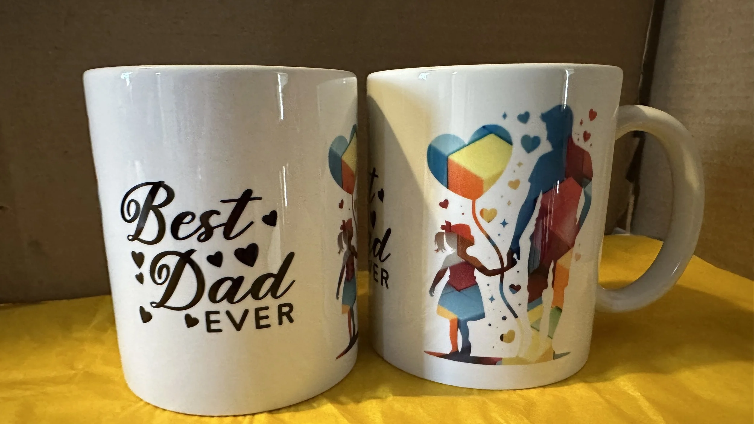 White ceramic mug with the text "Best Dad Ever" and a design of a father and child holding heart-shaped balloons, decorated with red, blue, orange, and yellow colors.