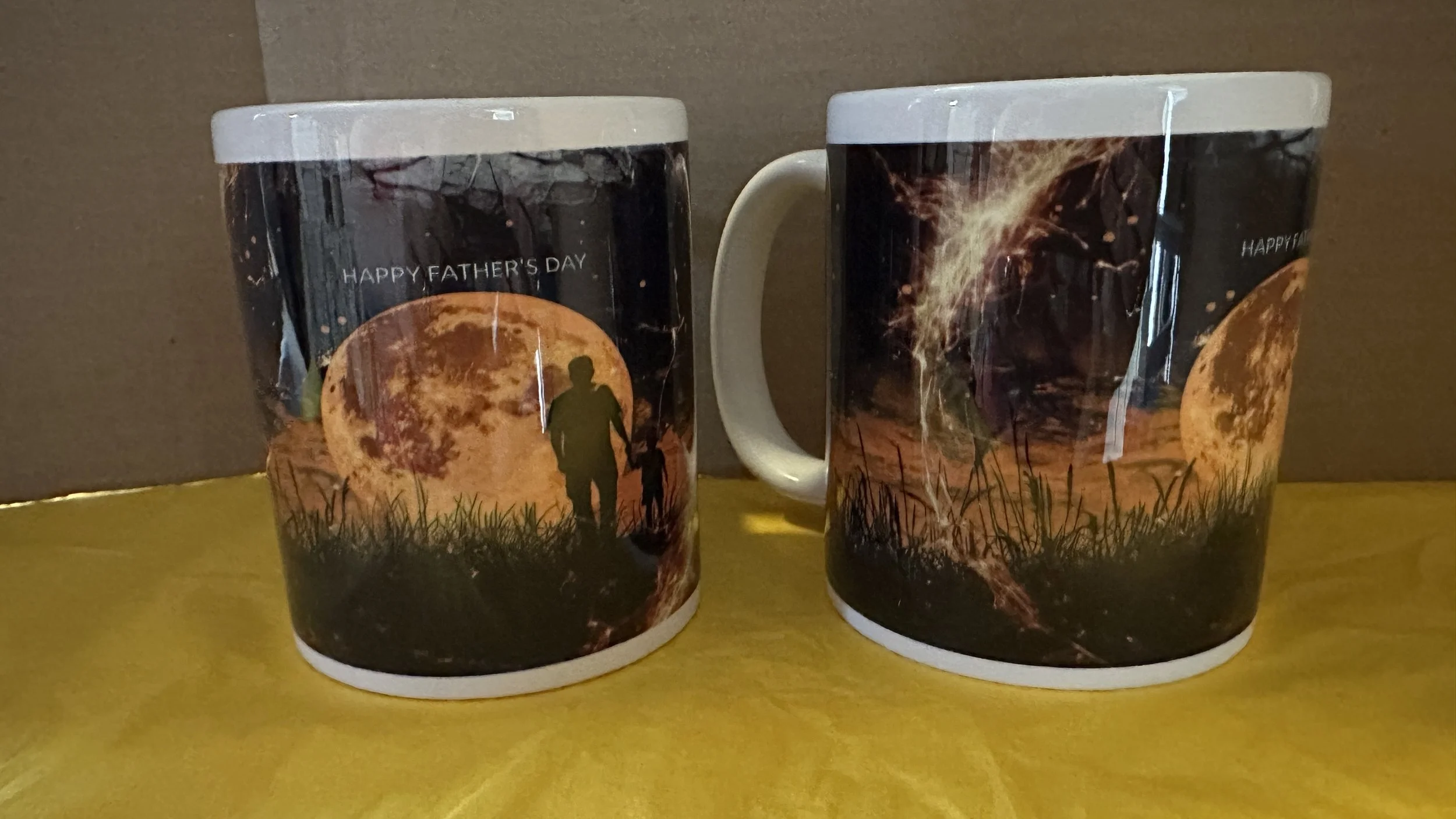 Two mugs with a Father's Day and moon-themed design, featuring a silhouette of a man and child walking, large moon, grass, firework, and text 'HAPPY FATHER'S DAY'.