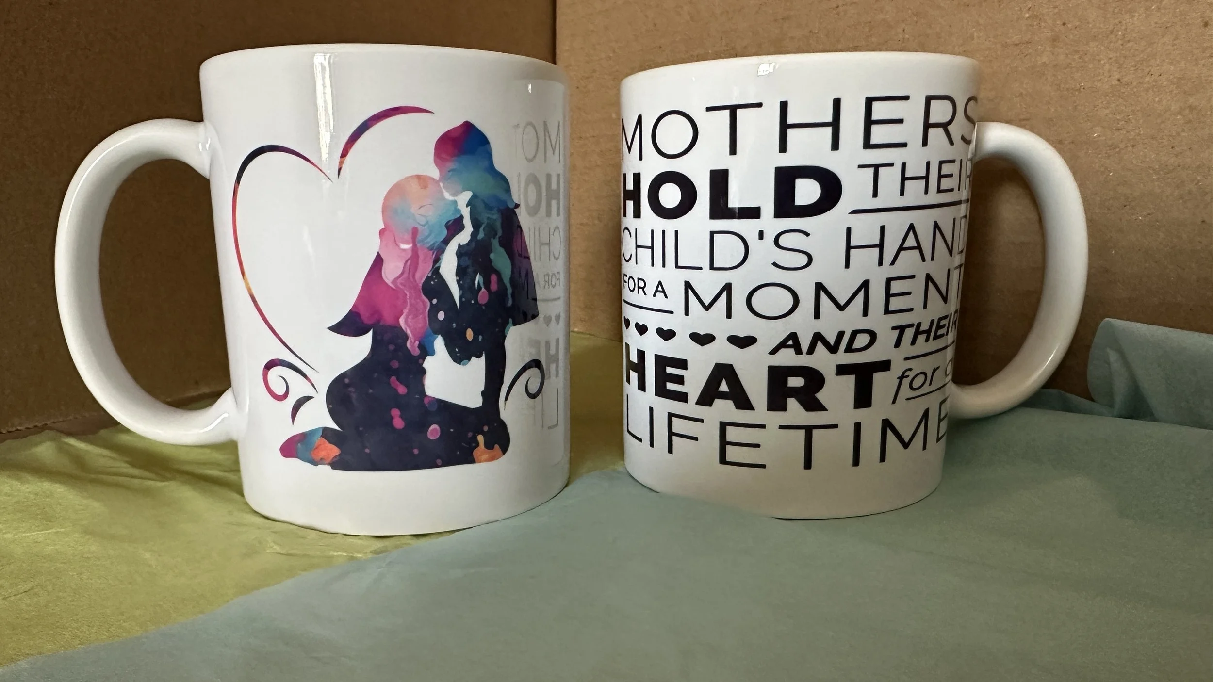 Two white ceramic mugs with printed designs placed on a yellow surface against a brown background.