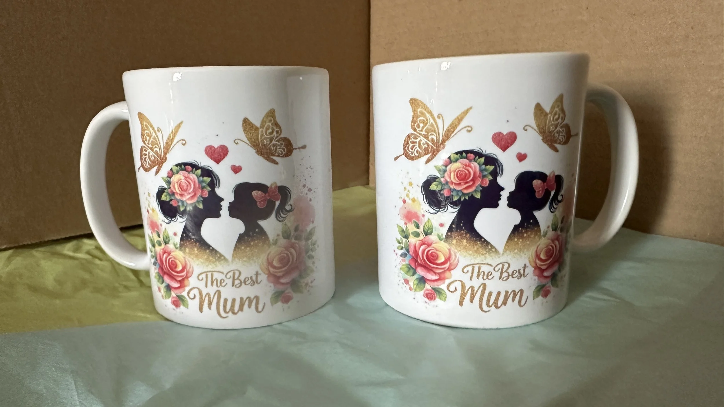 Two white mugs with floral and silhouette artwork, featuring the phrase 'The Best Mum' and images of two women with flowers and butterflies.
