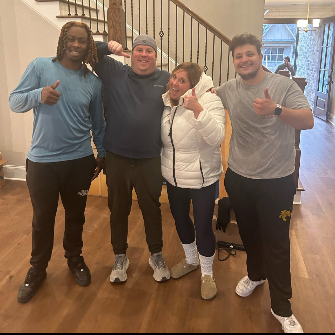 Four people standing indoors, smiling, and giving thumbs up gestures.