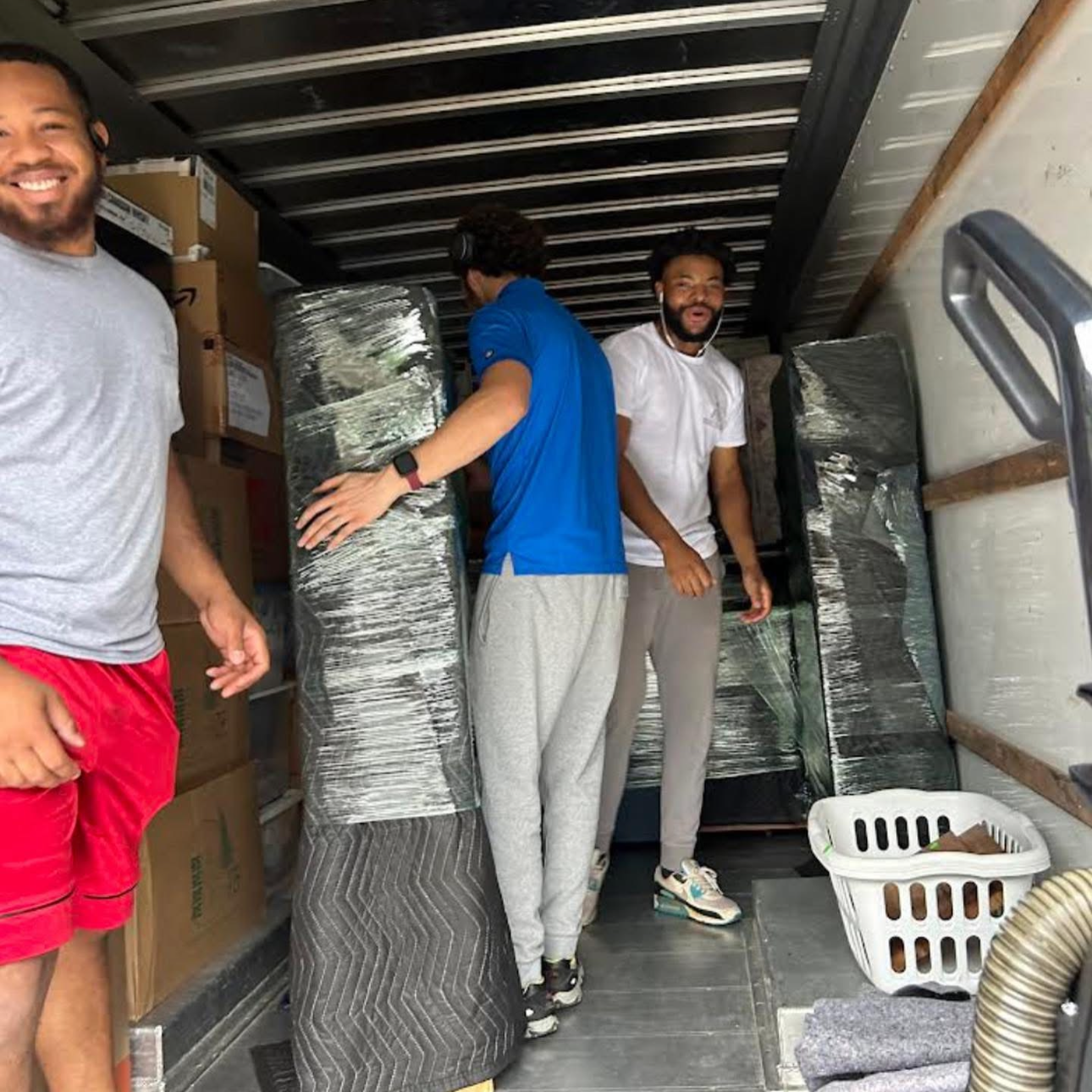 Three men loading or unloading items in the back of a truck. Two are smiling and appear to be in good spirits.