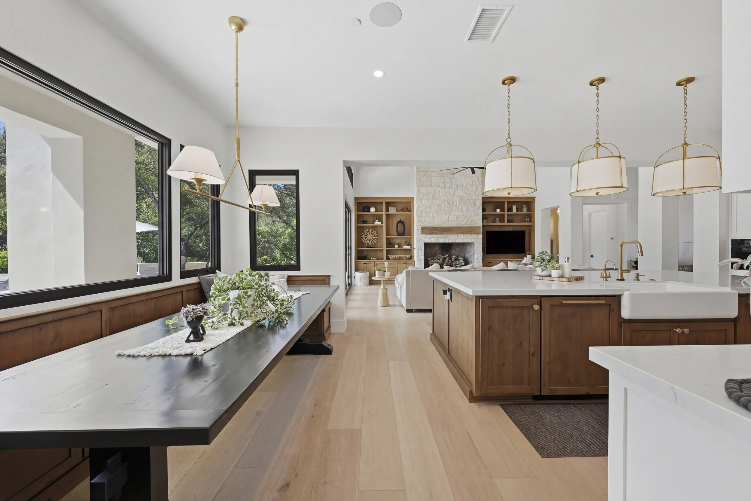 Open-concept kitchen and living room with large windows, white walls, wood floors, and modern lighting fixtures including pendant lights and a chandelier, featuring a white kitchen island, built-in shelving, and a fireplace.