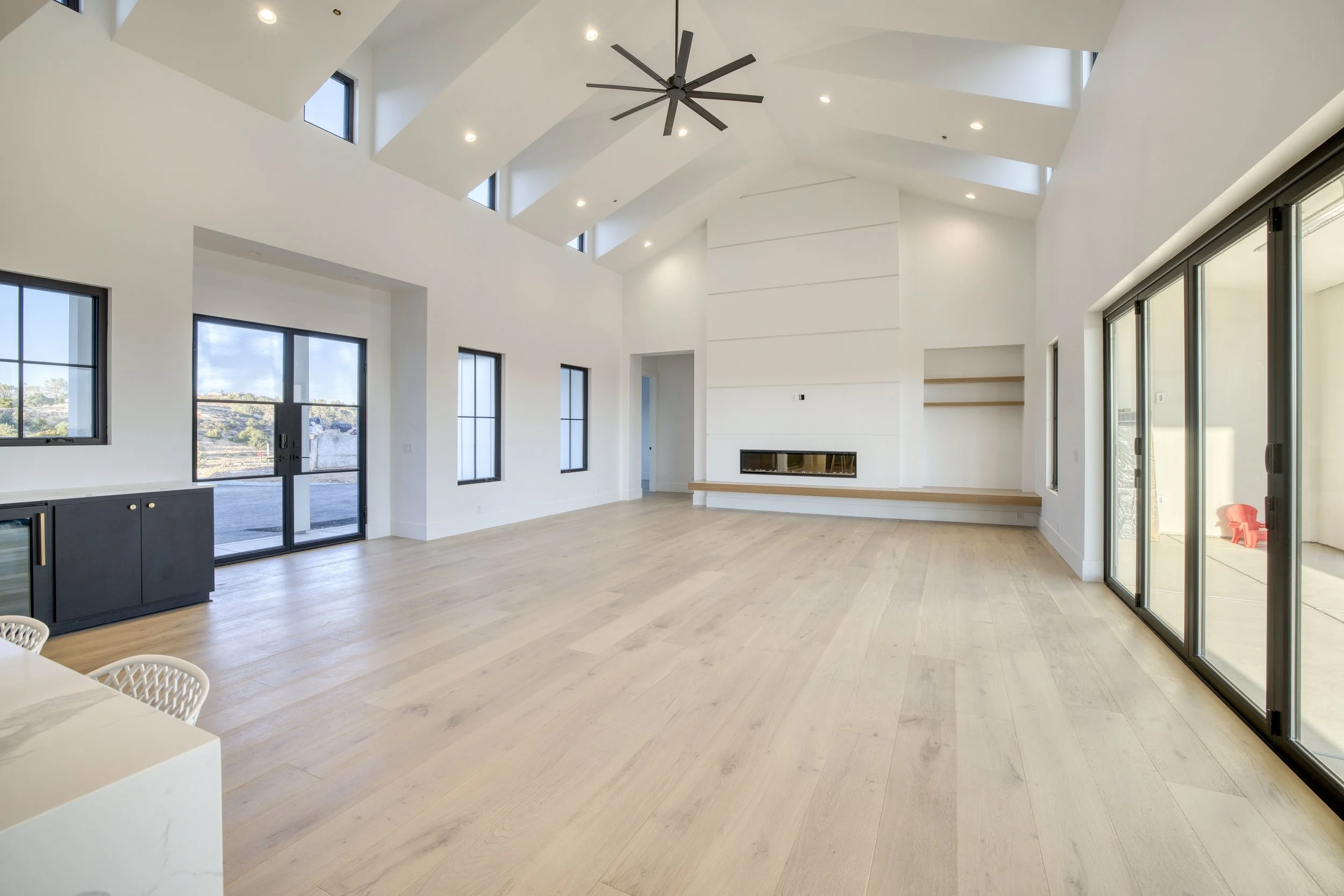 Modern living room with high vaulted ceiling, large windows, hardwood floors, fireplace, and sliding glass doors leading outside.
