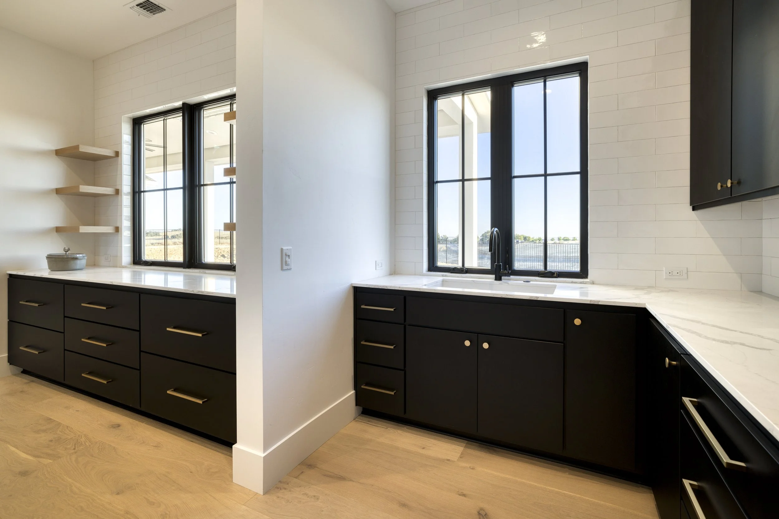 Modern kitchen with black cabinets, white marble countertops, black framed windows, and floating wood shelves on a white wall.