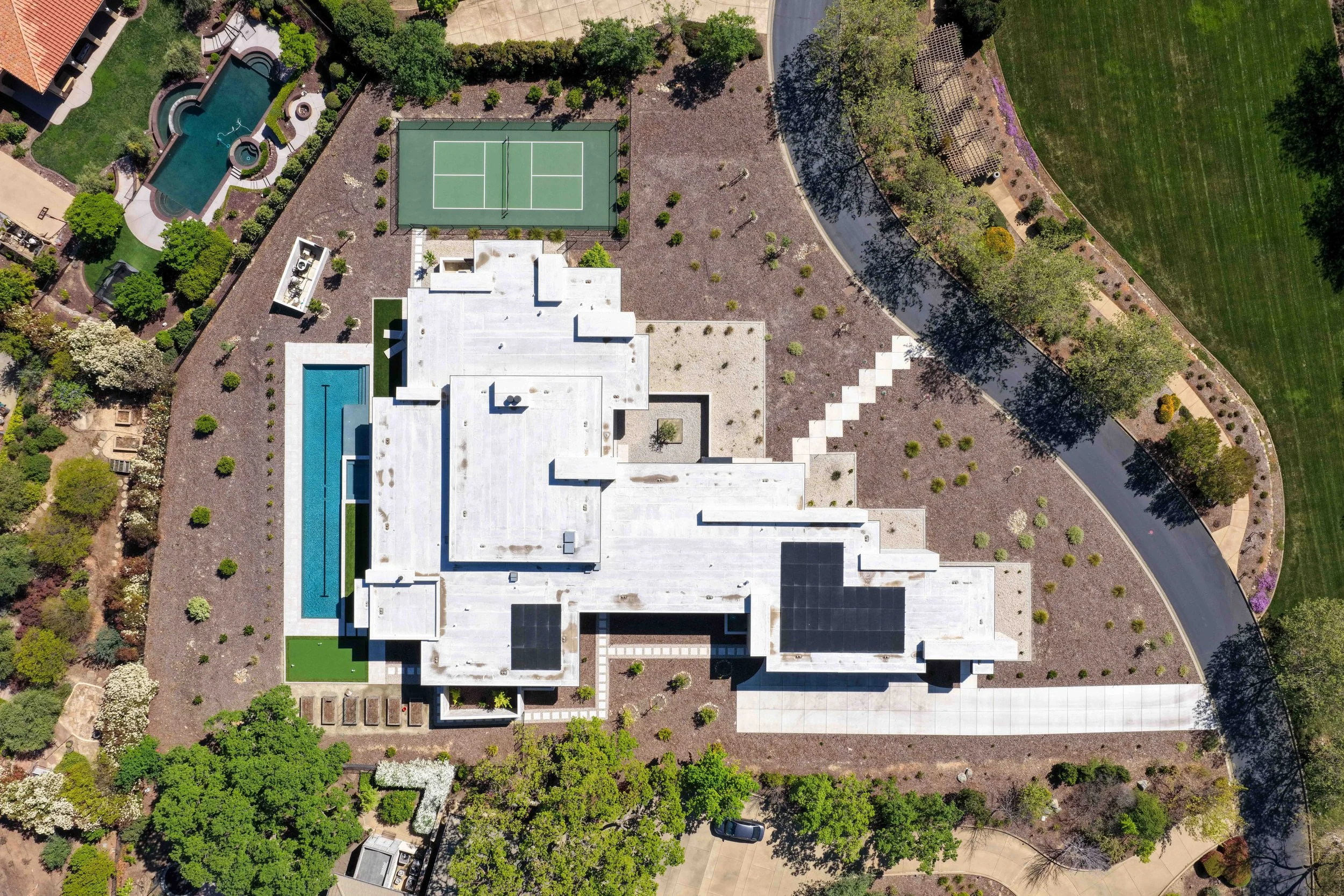 Aerial view of a modern white house with a swimming pool, tennis court, and landscaped yard with trees and pathways.